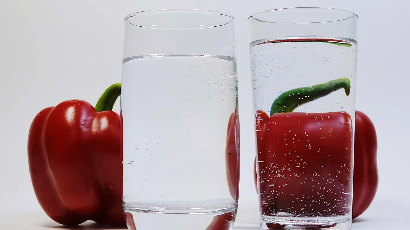 A red bell pepper behind a glass of water so that it looks distorted.