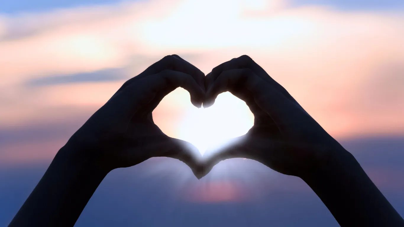 Hands making the shape of a heart in front of a sunset.